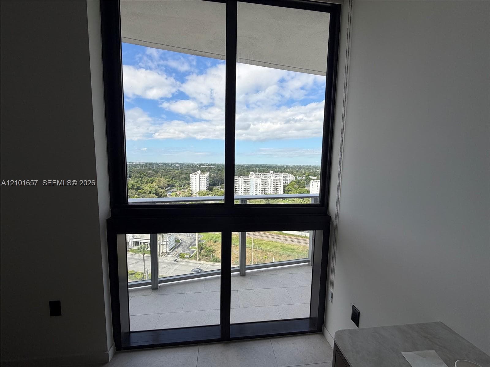 Floor-to-ceiling windows with dark metal framing and a tiled balcony featuring a glass railing
