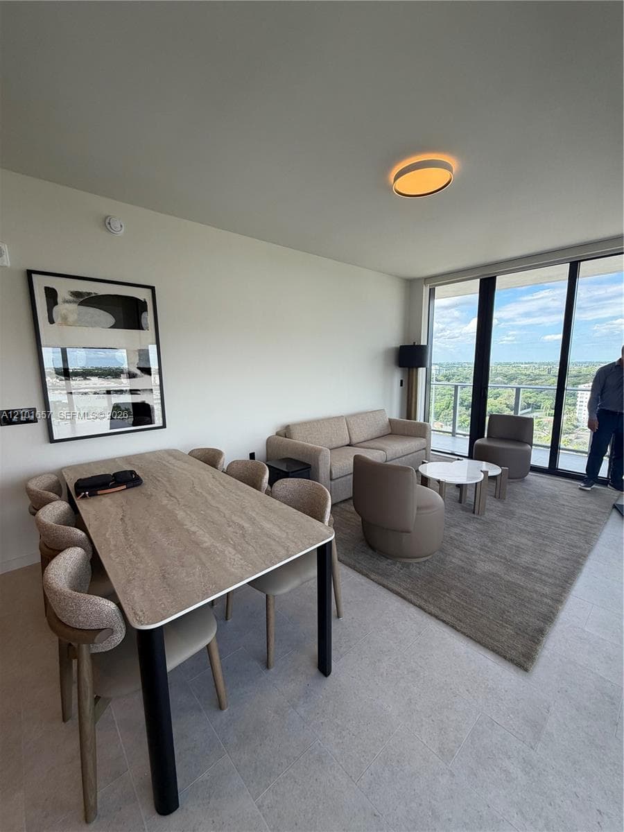 Open-concept interior featuring floor-to-ceiling glass windows, neutral tile flooring, modern circular ceiling lighting, and a glass-railed balcony