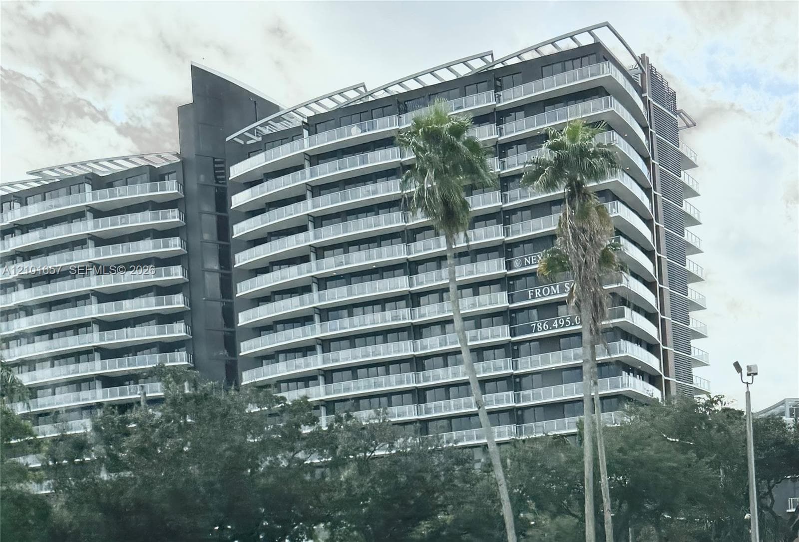 Modern high-rise exterior featuring a dark metallic facade, rhythmic rows of glass-railed balconies, and a stepped roofline