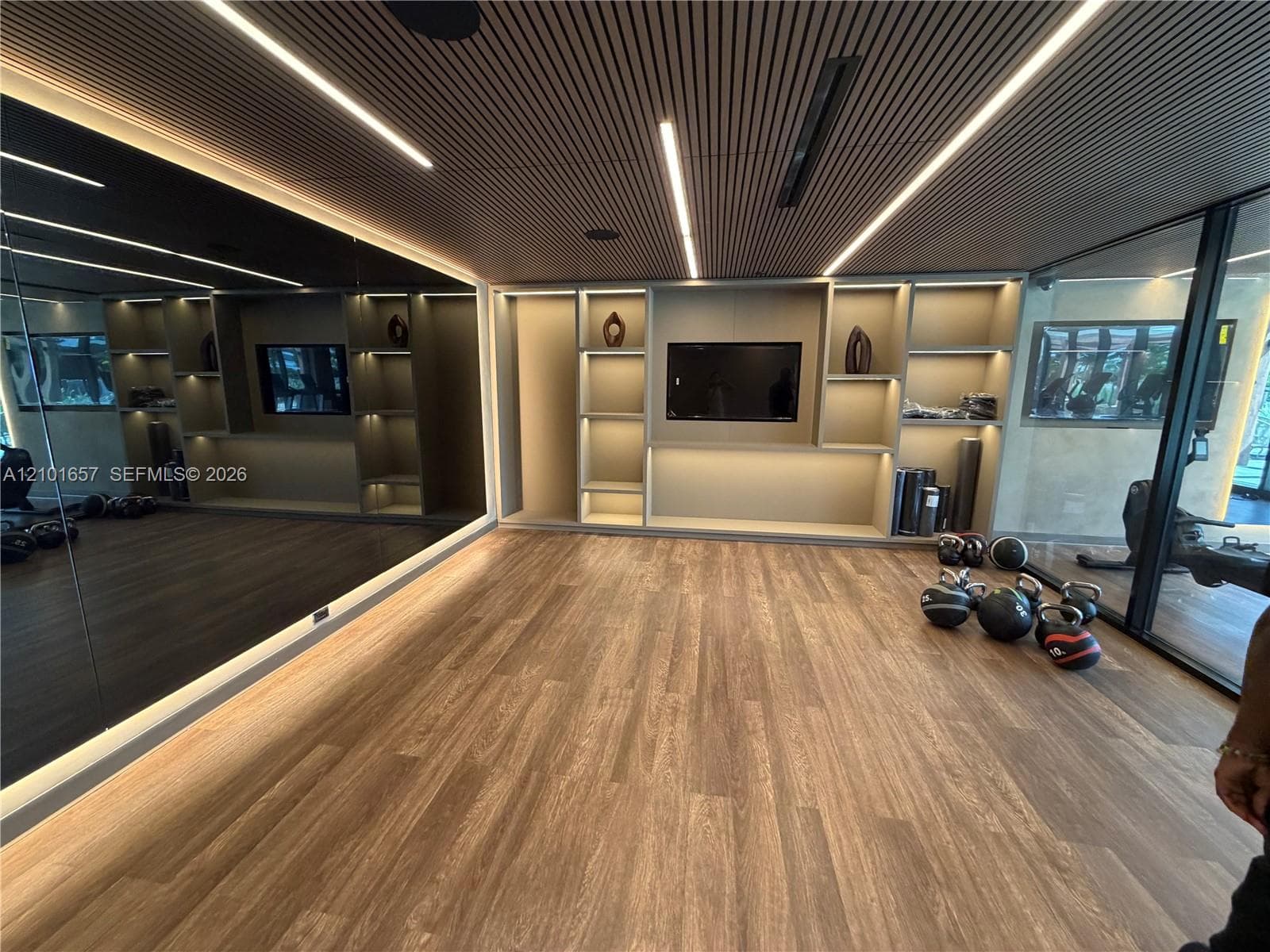 Slatted wood ceiling with recessed linear lighting, full-height wall mirror, wood-finish flooring, and built-in display shelving featuring integrated LED accent lighting