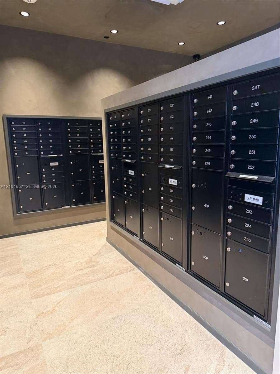 Integrated mail station featuring matte black secure postal lockers, neutral stone-finish tile flooring, recessed ceiling lighting, and smooth, monochromatic wall finishes