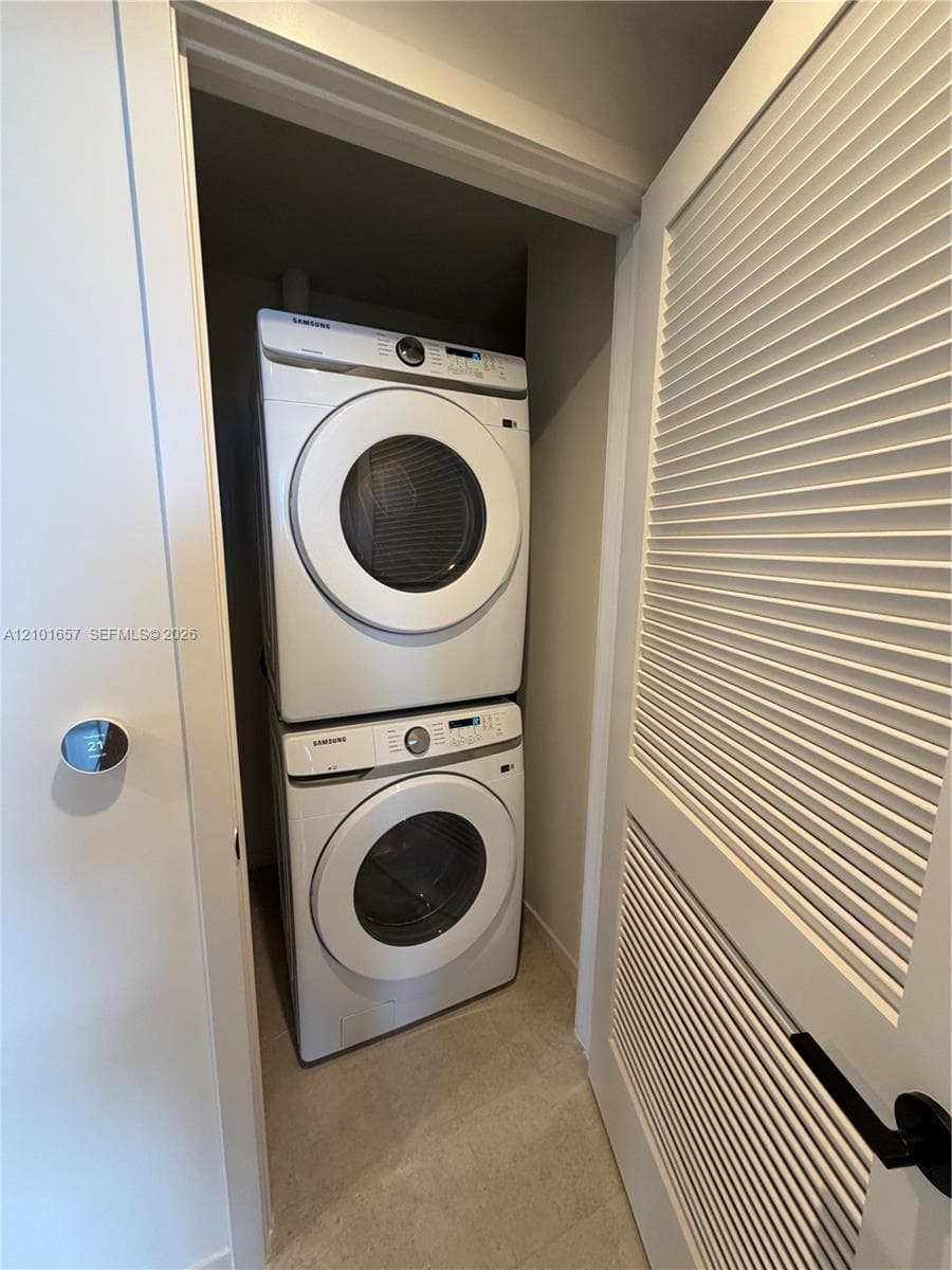 Stacked laundry center featuring high-efficiency washer and dryer, tile flooring, and louvered closet door
