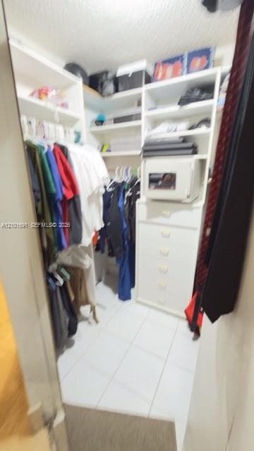 Walk-in closet featuring white built-in shelving, integrated storage drawers, and tile flooring