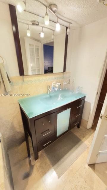 Dark wood-finish vanity with frosted glass paneling, topped with a translucent blue integrated glass countertop and basin, featuring a wall-mounted multi-light fixture and a large rectangular mirror with a dark trim