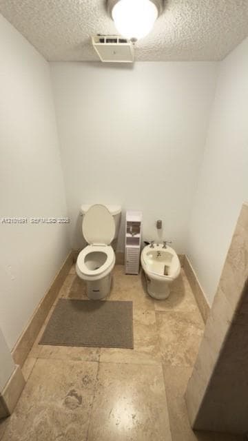 Enclosed water closet featuring tile flooring, a porcelain toilet, and a bidet