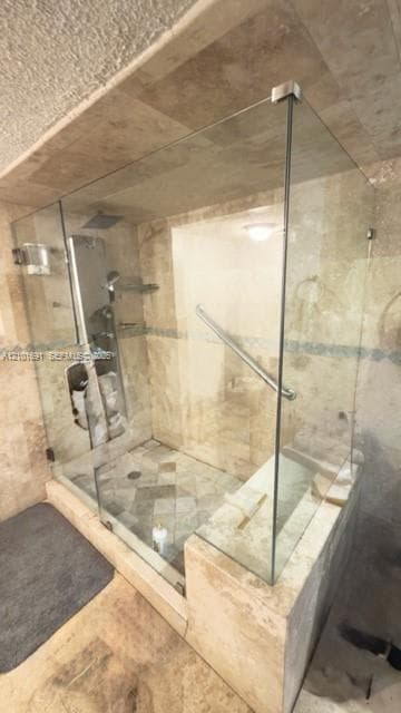 Walk-in shower featuring a frameless glass enclosure, natural stone tile surround, integrated stone bench, overhead rainfall showerhead, and a wall-mounted metal grab bar