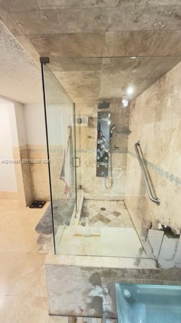 Walk-in shower featuring natural stone tile wall and floor surfaces, glass partition, integrated stainless steel shower panel, and wall-mounted grab bar