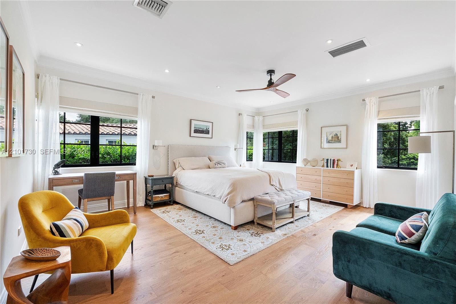 Neutral-toned bedroom featuring wood-finish flooring, multi-pane black-trimmed windows, and a ceiling fan with integrated lighting