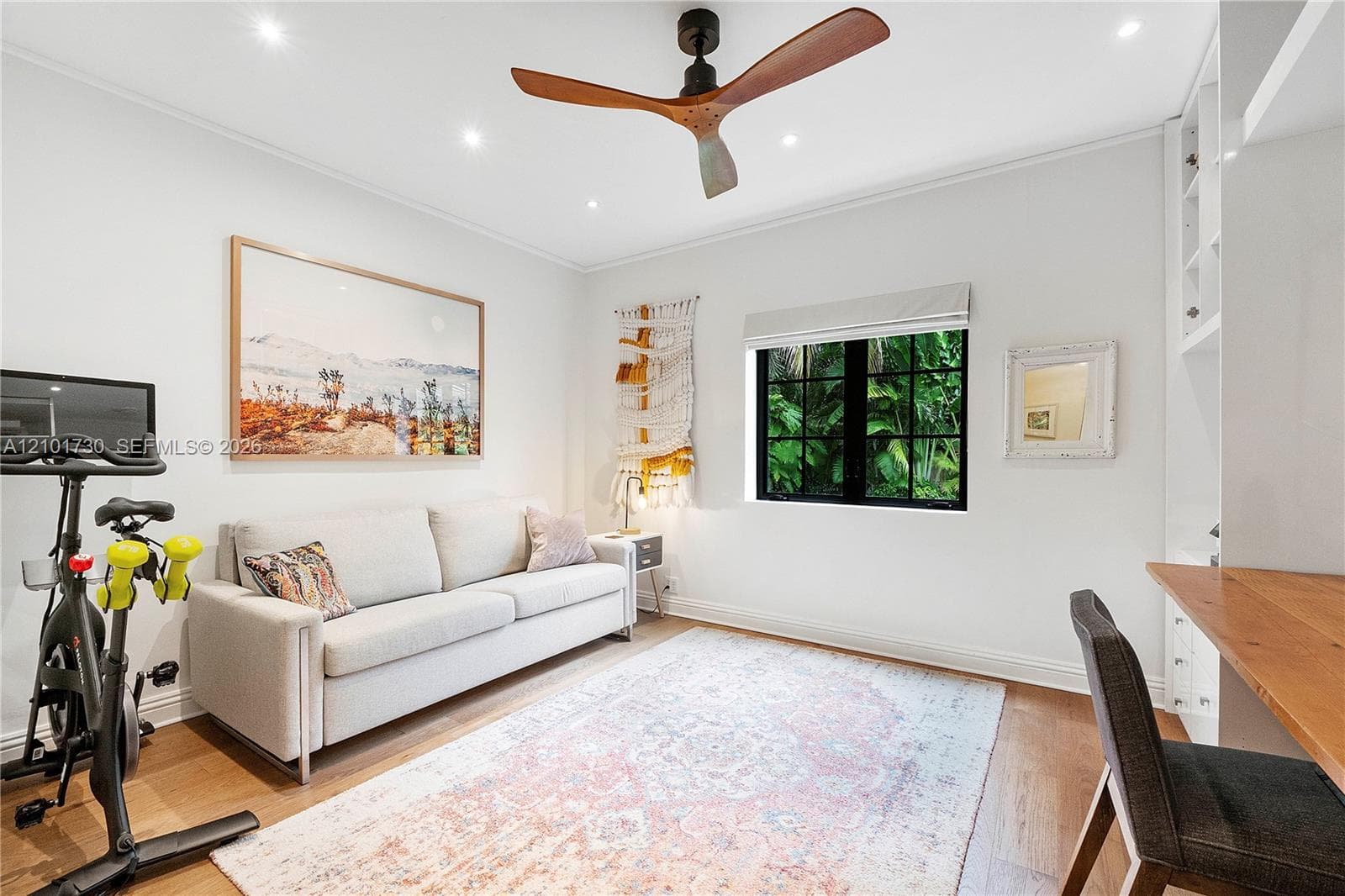 Room featuring wood-finish flooring, a modern three-blade ceiling fan, recessed lighting, a multi-pane black-framed window, and built-in shelving with an attached wooden desk surface