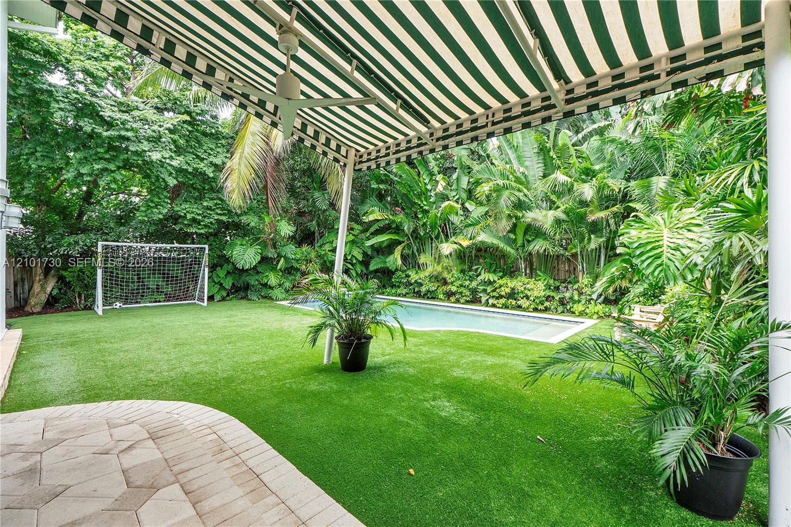 Backyard featuring a paver patio, a retractable striped awning, an in-ground pool, and synthetic turf