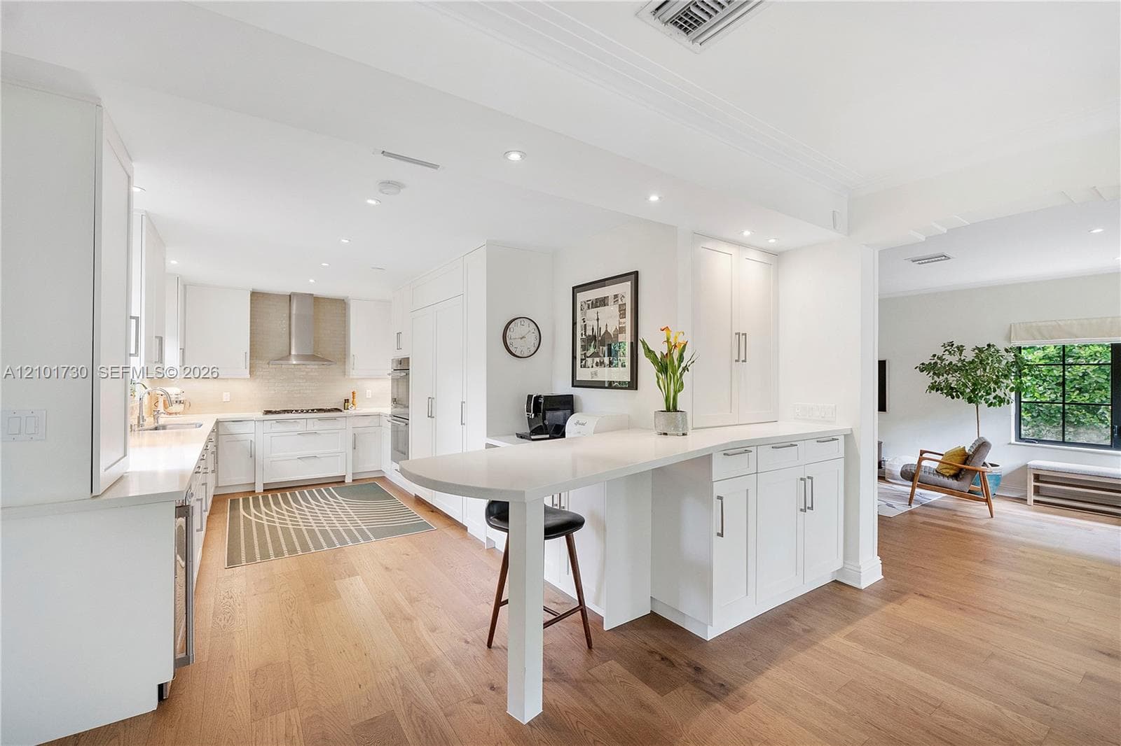 Kitchen featuring white shaker-style cabinetry, quartz countertops, integrated peninsula, stainless steel range hood, and wood-finish flooring