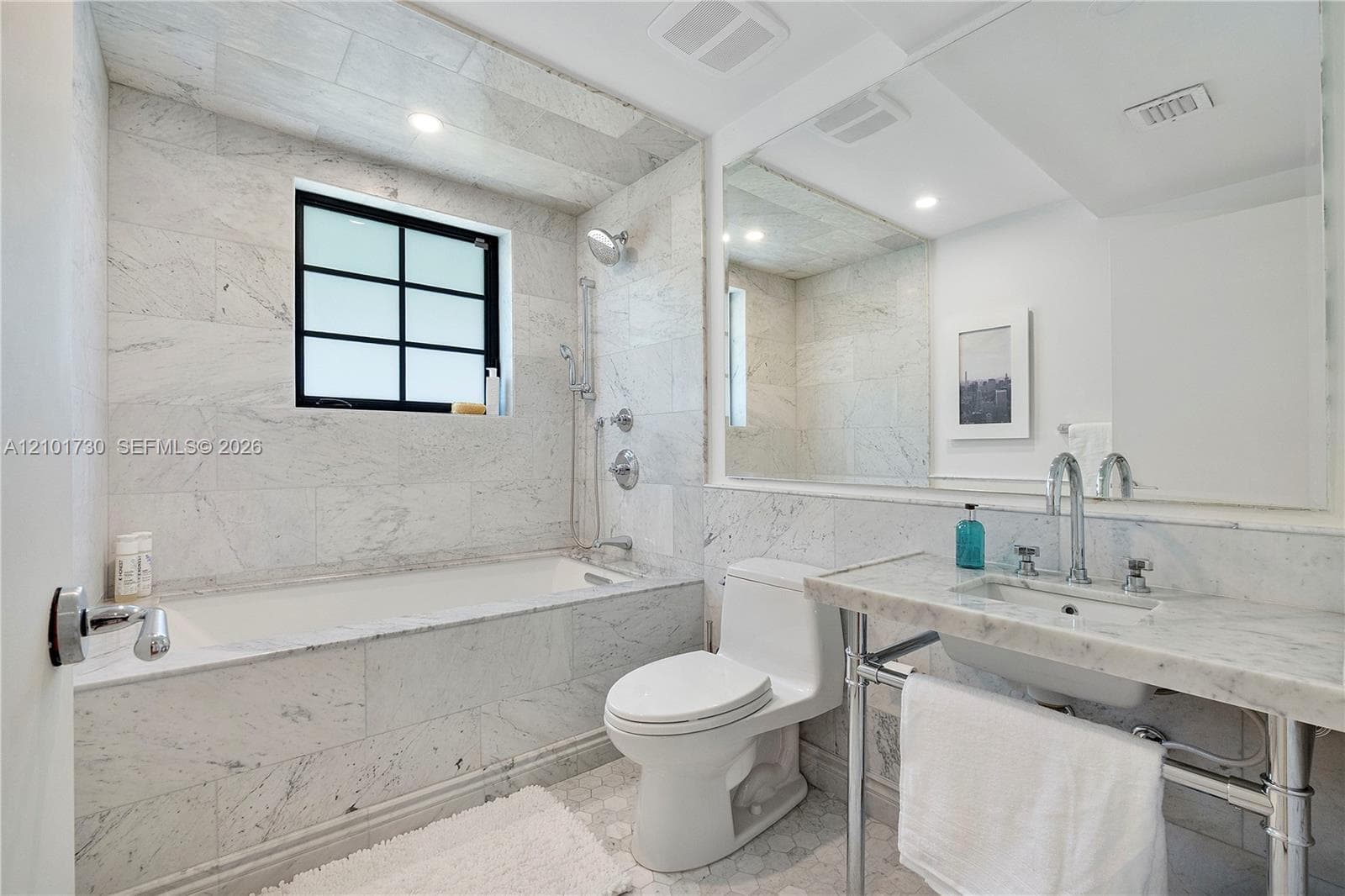Bathroom featuring stone tile surround, tub with handheld shower fixture, stone-topped console vanity with integrated basin, polished chrome plumbing fixtures, and wall-to-wall mirror