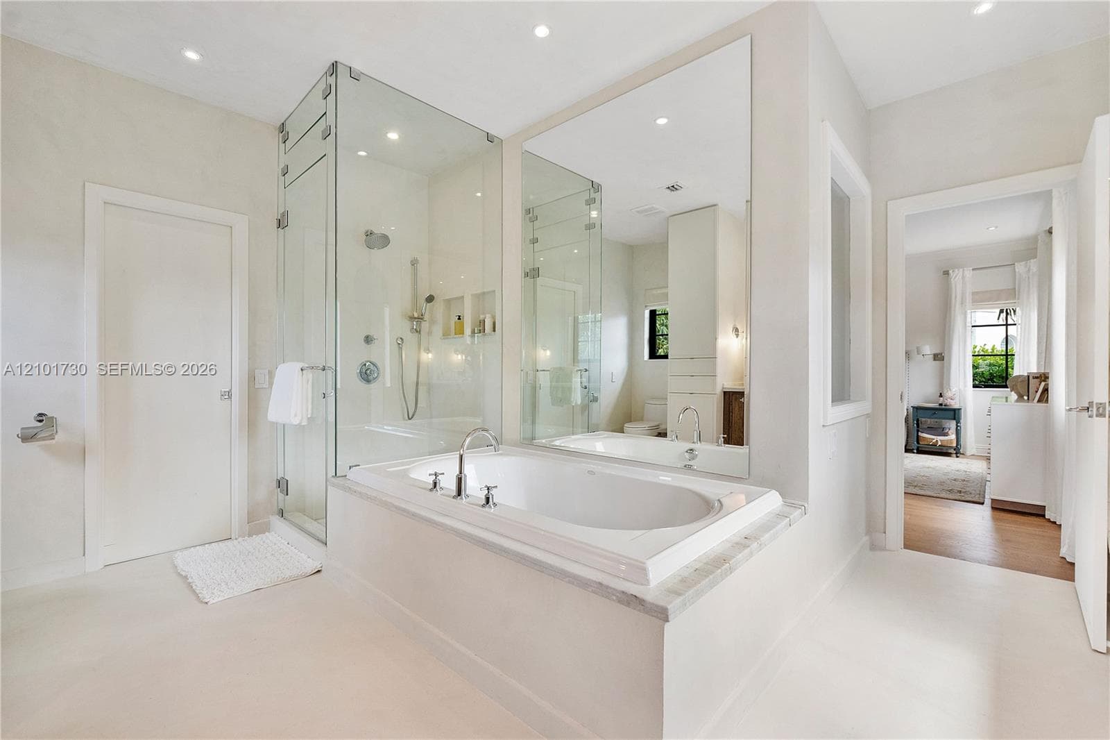 Soaking tub with a stone-surround deck, glass-enclosed walk-in shower, wall-to-wall mirror, and recessed lighting