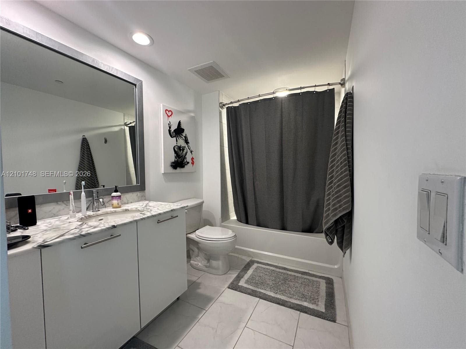 White vanity with a stone countertop, featuring an undermount sink and a framed mirror
