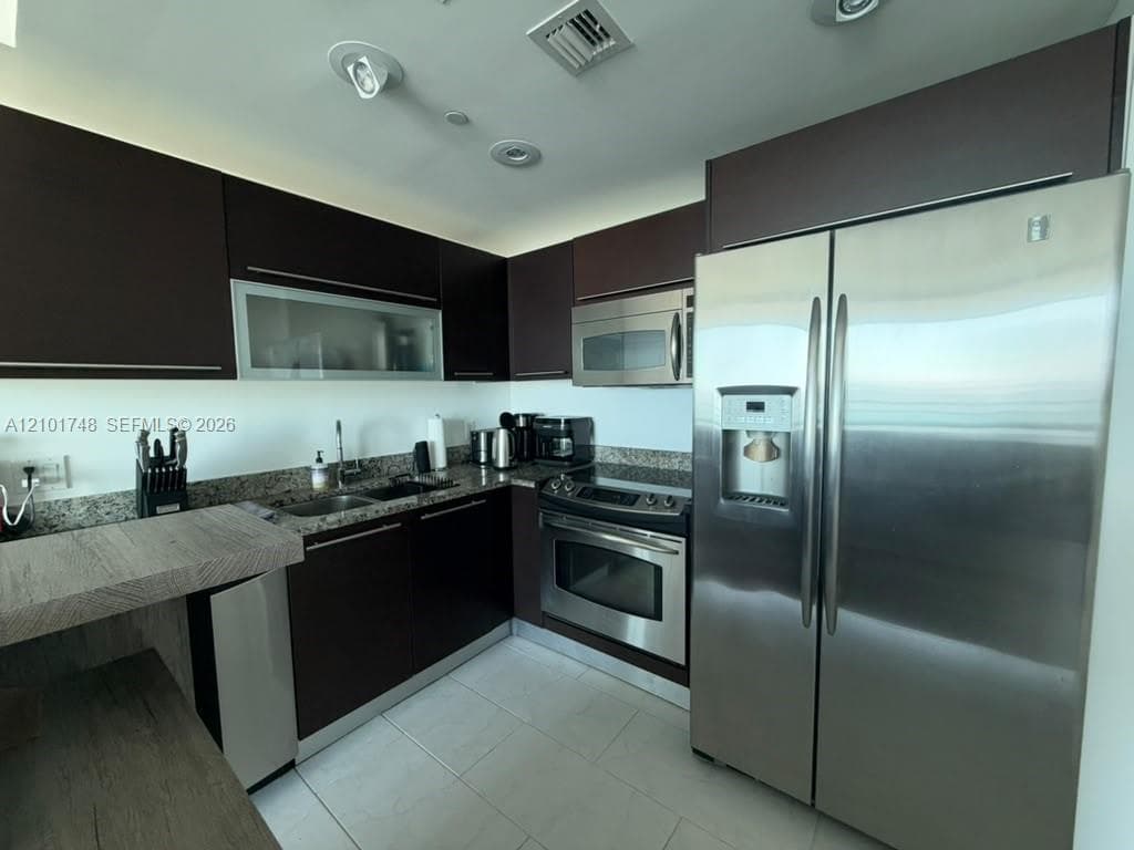 Modern kitchen featuring stainless steel appliances, dark wood-finish cabinetry, granite-style countertops, and tile flooring