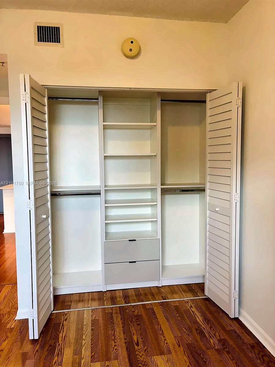 Built-in closet system featuring dual louvered doors, integrated shelving, double hanging rods, and two lower drawers with matte hardware