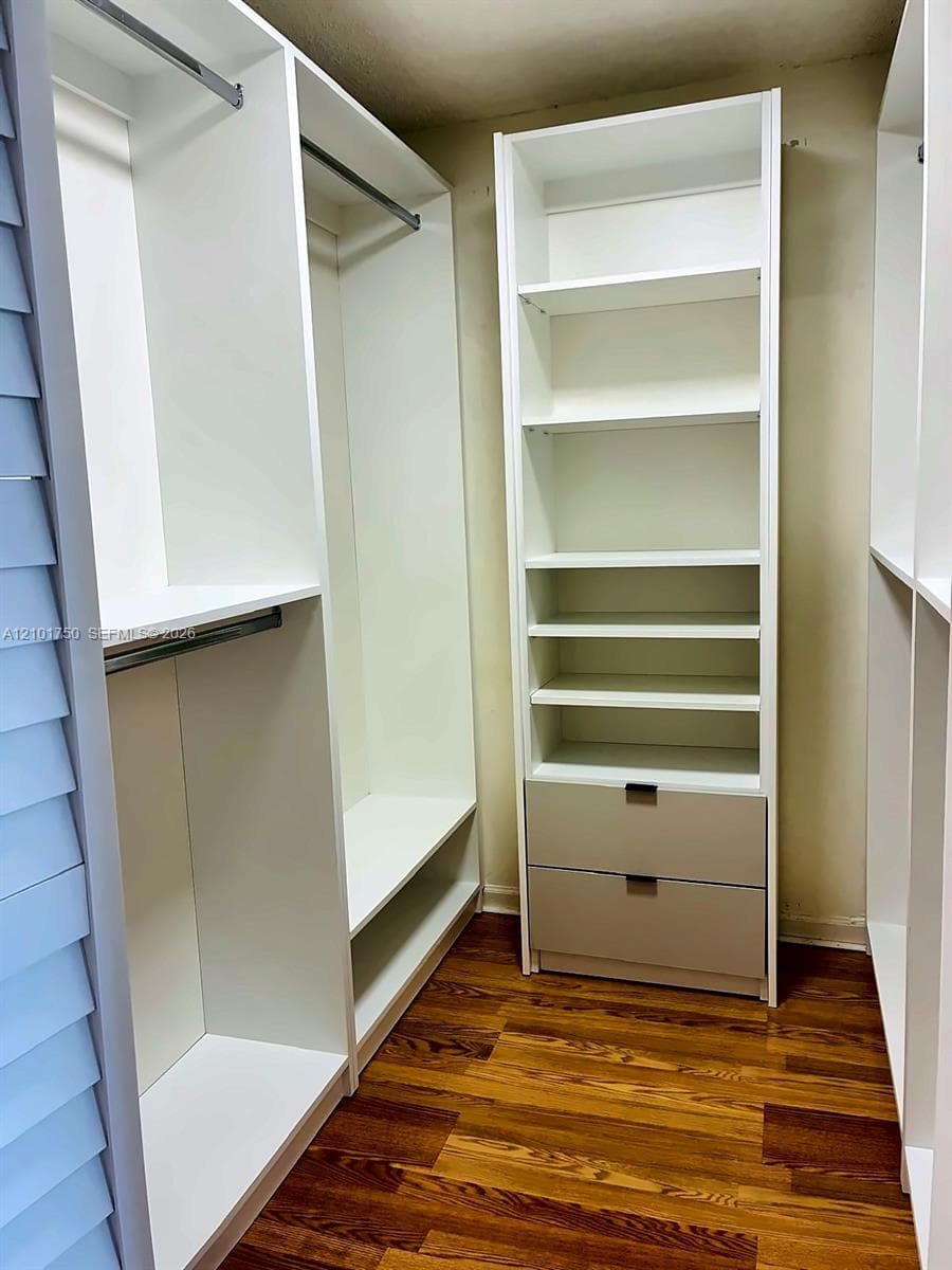 Custom walk-in closet featuring white built-in shelving, dual hanging rods, stacked storage drawers with matte hardware, and wood-finish flooring