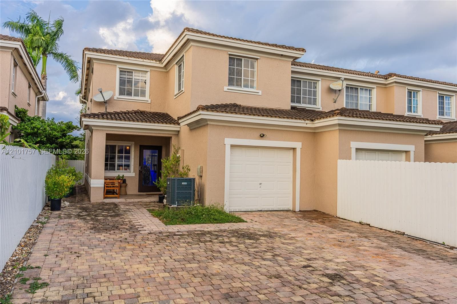 Stucco exterior with a terracotta tile roof, paver driveway, and an attached garage