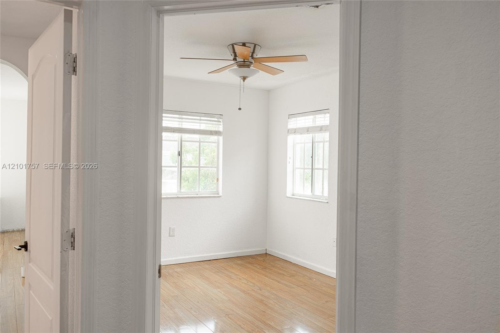 Wood-finish flooring with a ceiling fan light fixture and two windows with blinds