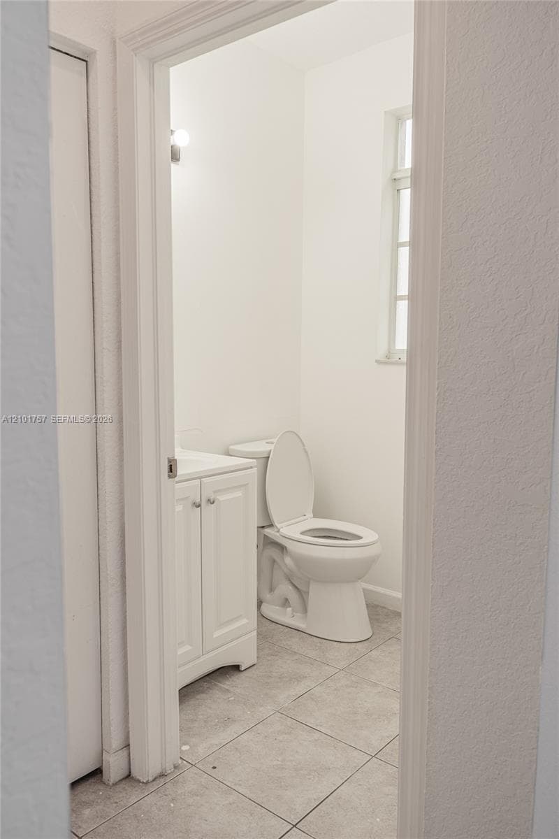 White vanity with dual cabinet doors, light-toned tile flooring, and a window