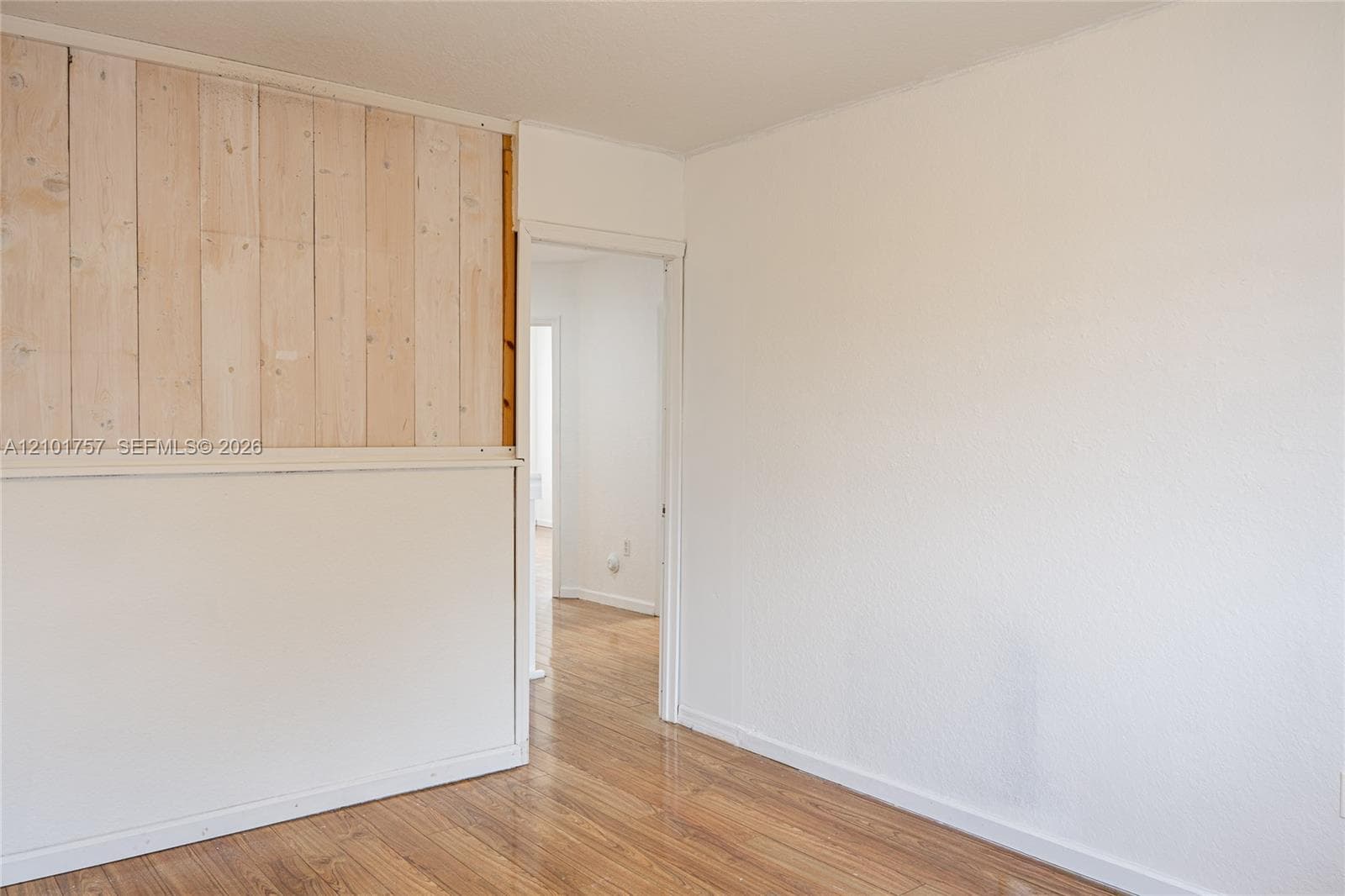 Wood-finish flooring with a light sheen, white painted walls, and an accent wall featuring vertical wood paneling