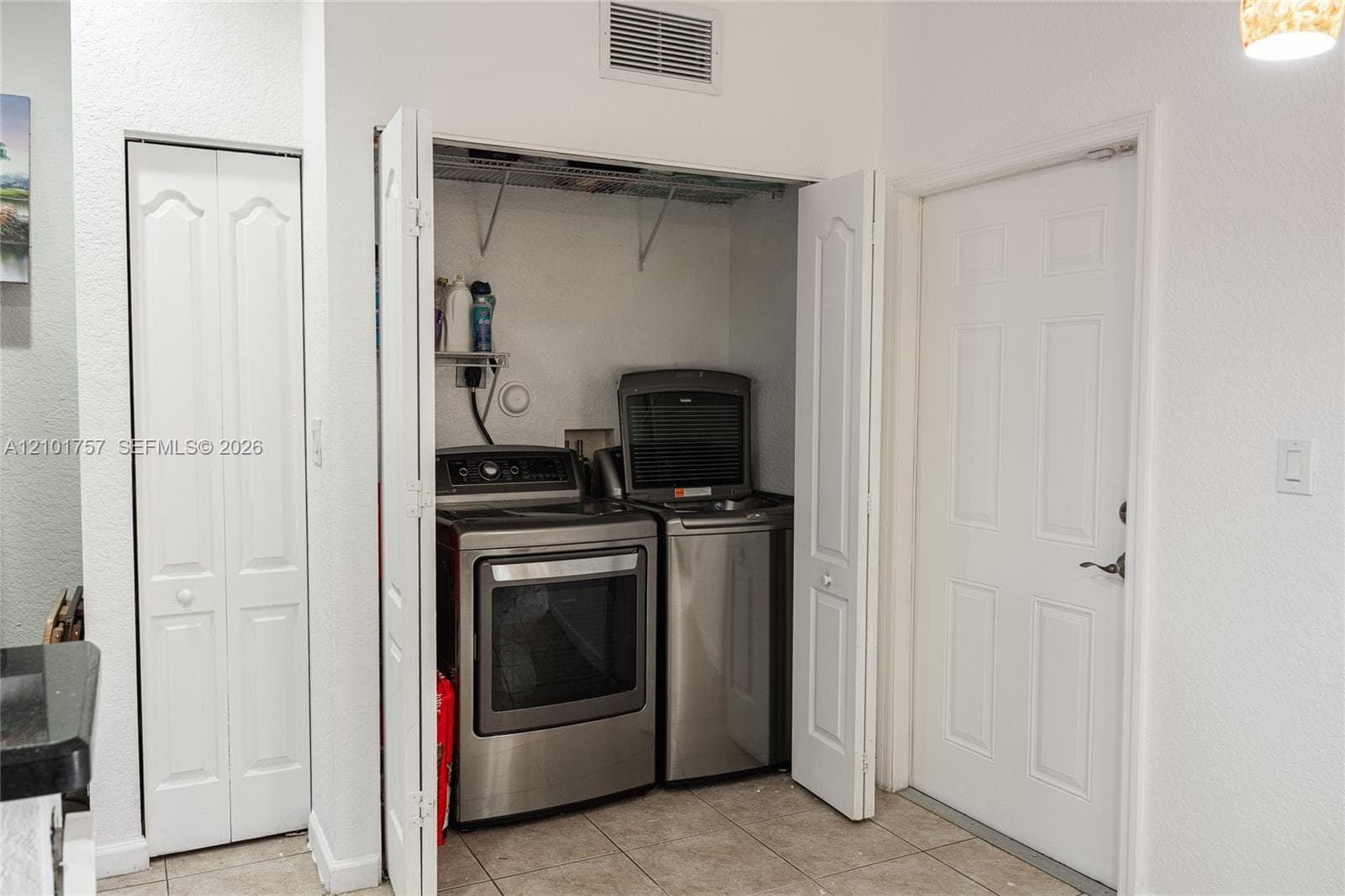 Laundry closet featuring bi-fold doors, tiled flooring, and stacked appliances