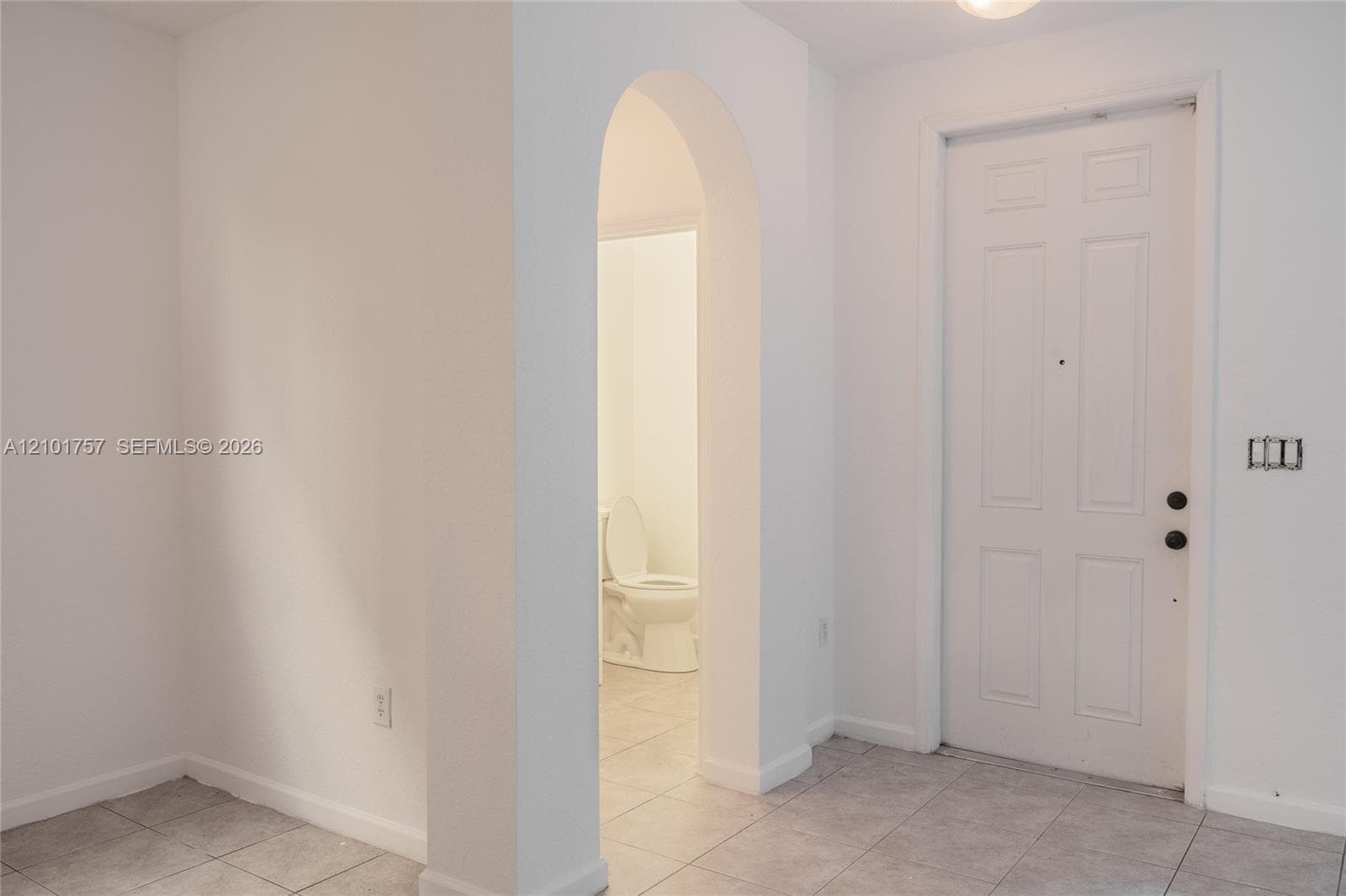 White paneled door, arched doorway, and light-toned tile flooring