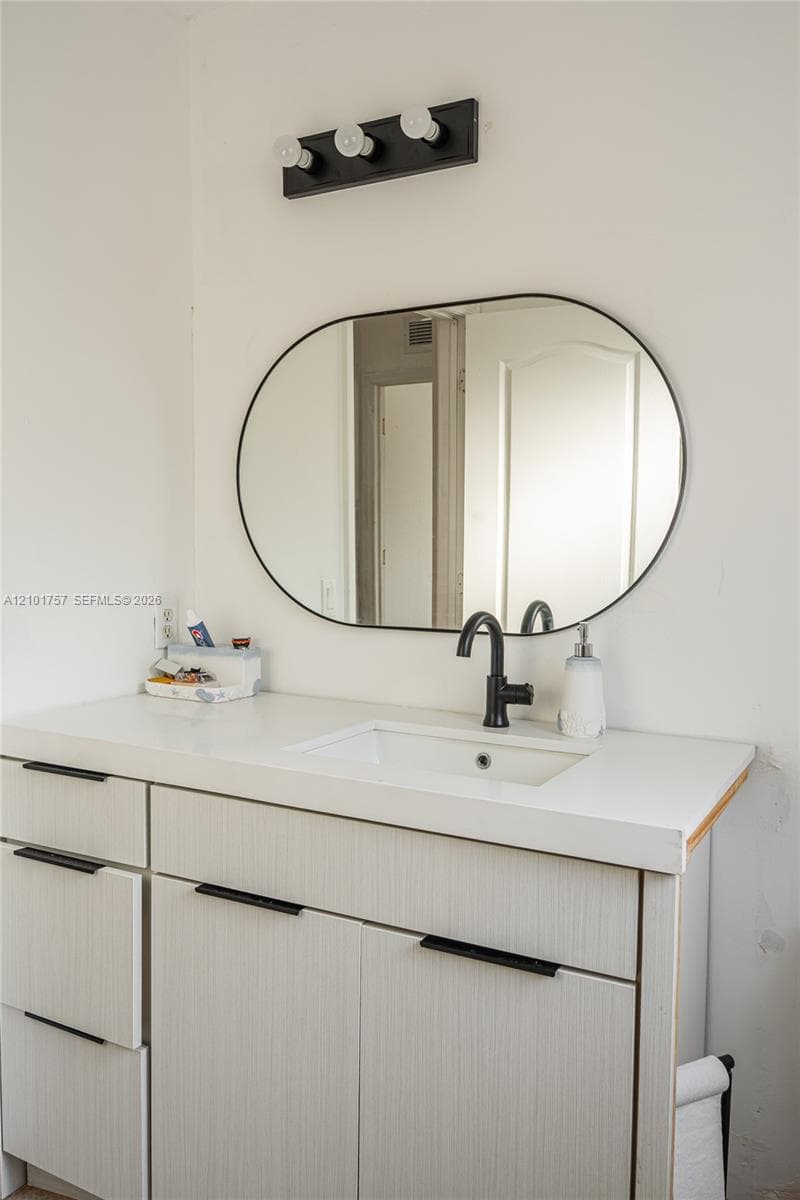 Vanity with white finish cabinetry, integrated sink, and matte black faucet