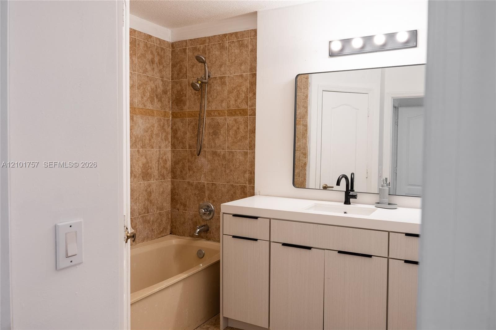 Tile-surround shower with a built-in tub, light wood-finish vanity with ample storage, integrated rectangular sink, wall-mounted mirror, and modern lighting fixture