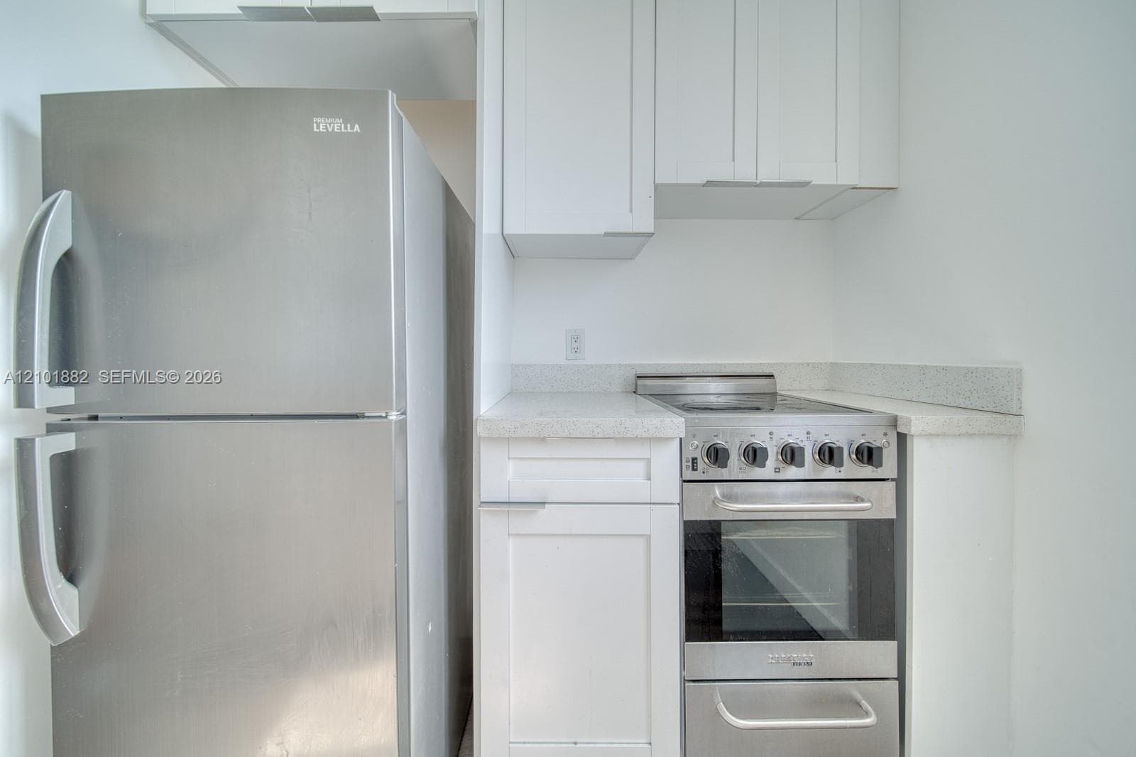 Kitchen featuring white shaker-style cabinetry, speckled stone-finish countertops, and stainless steel appliances including a refrigerator and a slide-in range