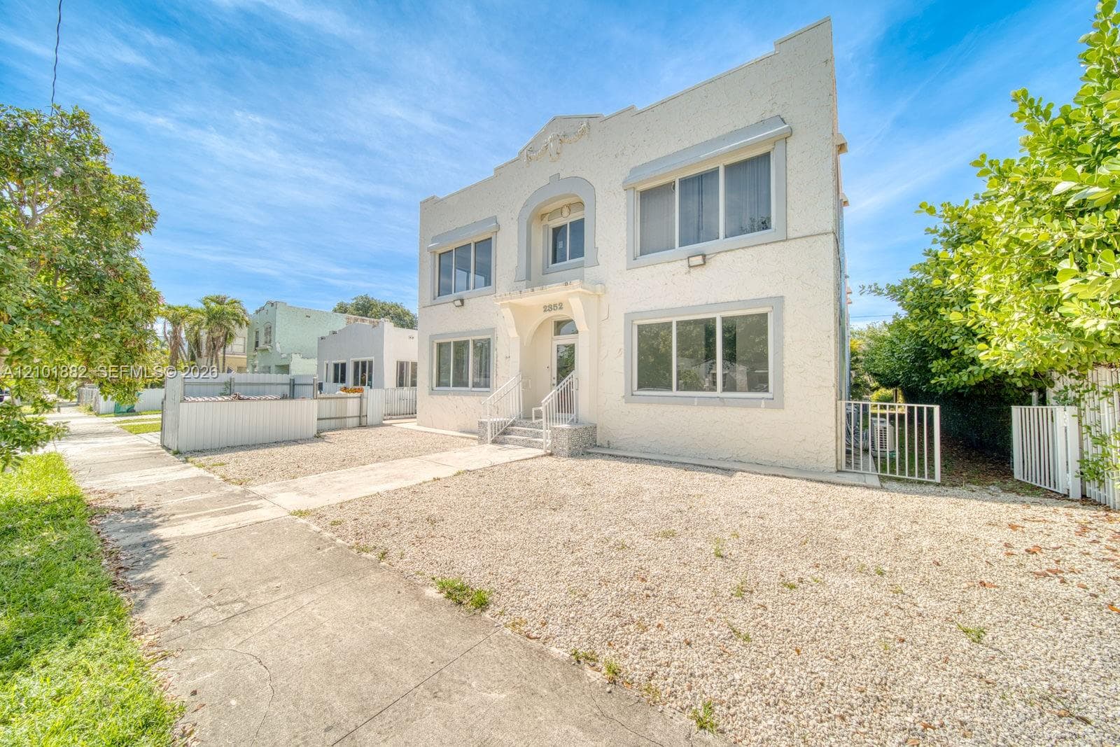 Multi-story exterior featuring textured stucco facade, decorative parapet molding, arched entryway, and large multi-pane windows