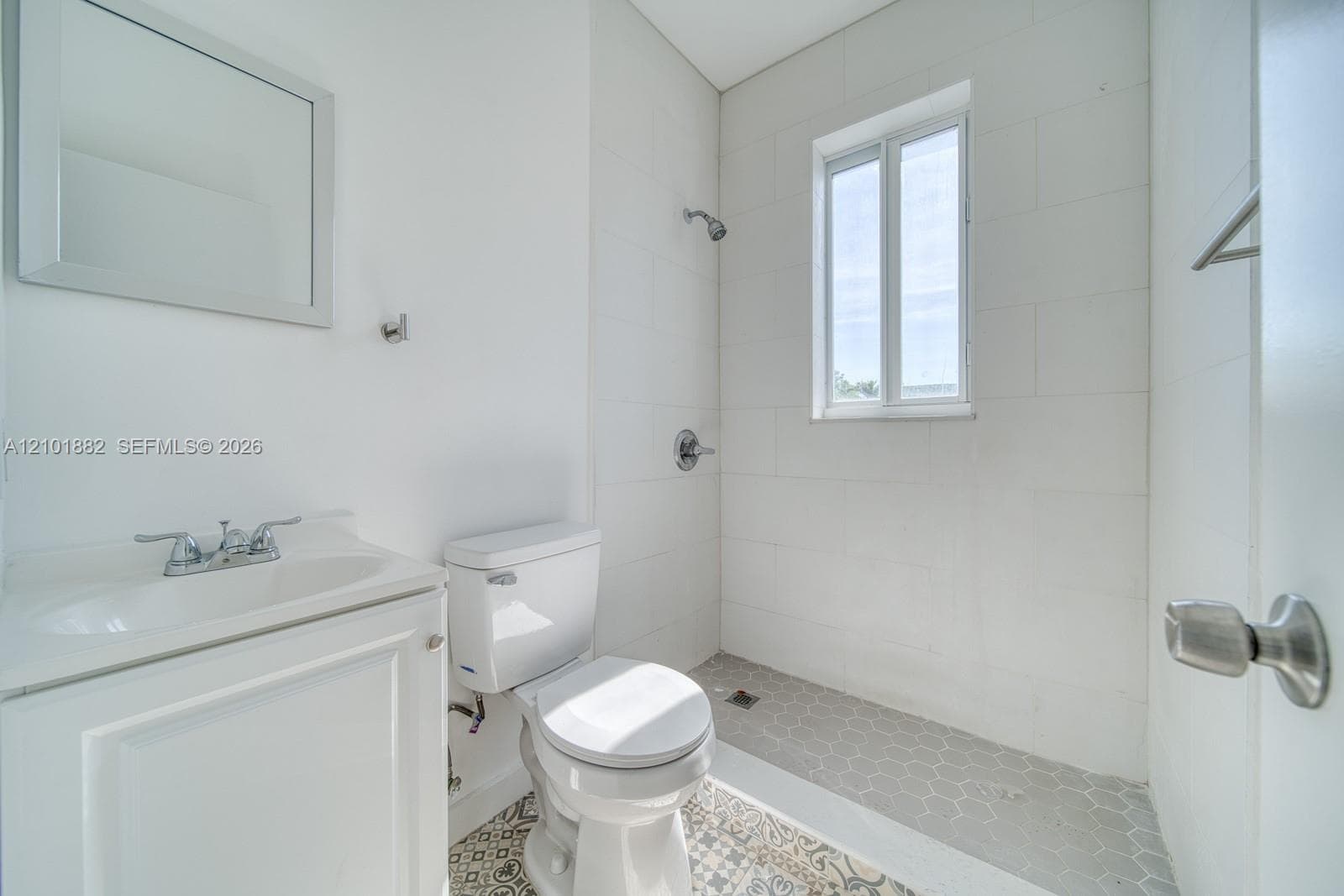 Bathroom featuring a white vanity cabinet, a wall-mounted mirror, a tiled shower enclosure, and patterned floor tile