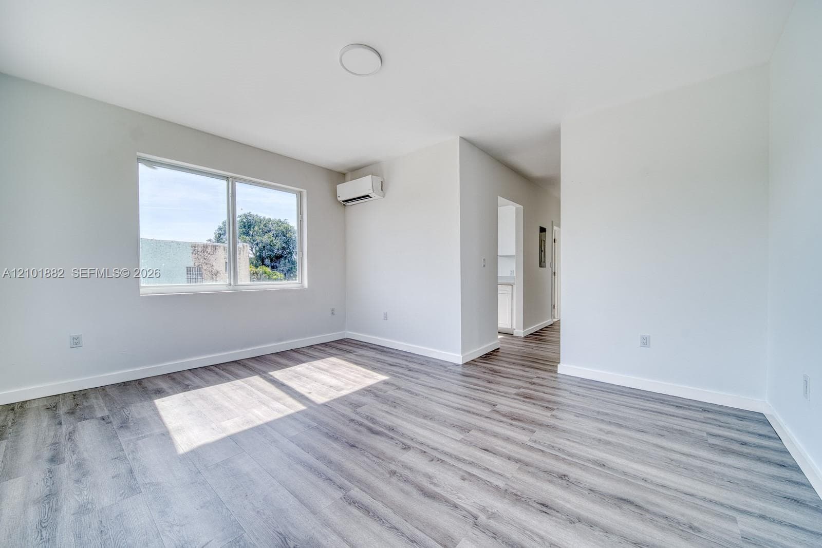 Bright interior space featuring wood-finish flooring, a wall-mounted climate control unit, and a large window