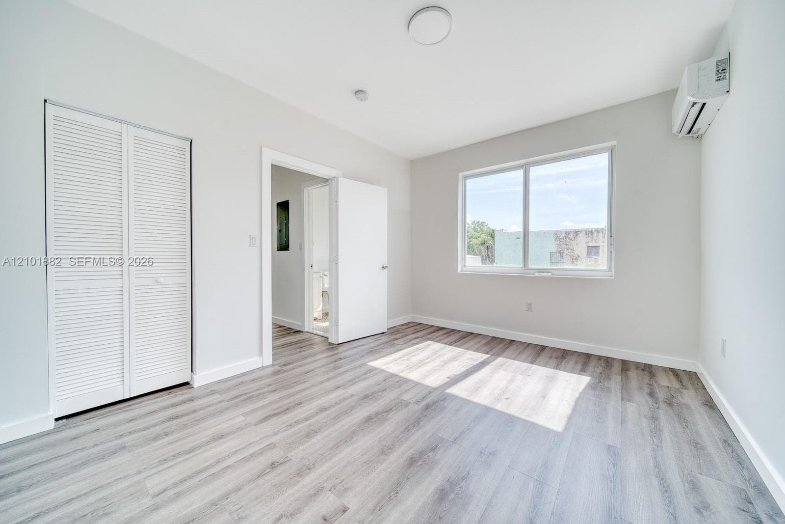 Room featuring wood-finish flooring, a wall-mounted ductless air conditioning unit, sliding window with exterior view, and a closet with bifold louvered doors