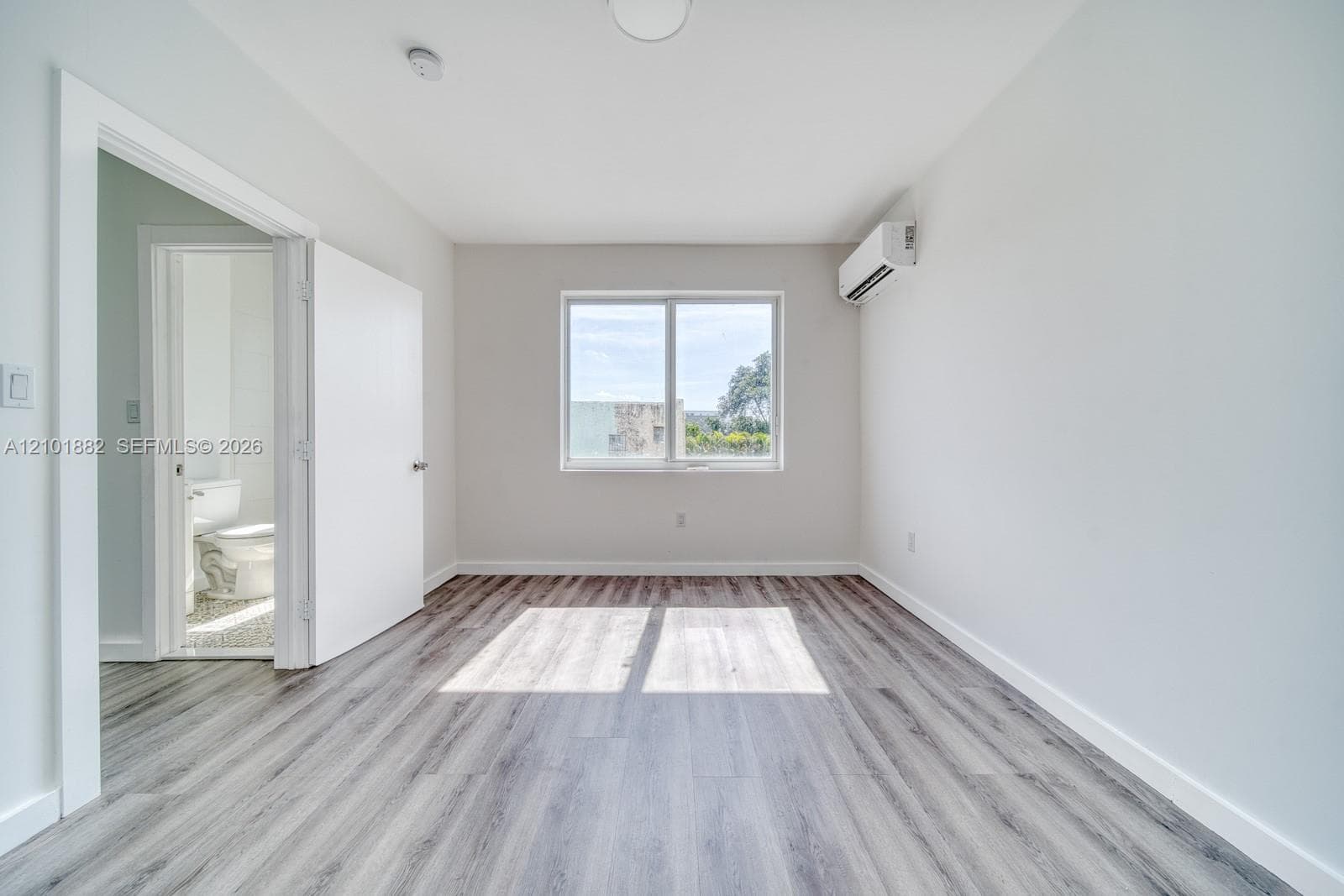 Interior space featuring wood-finish flooring, a wall-mounted ductless climate control unit, and a large window