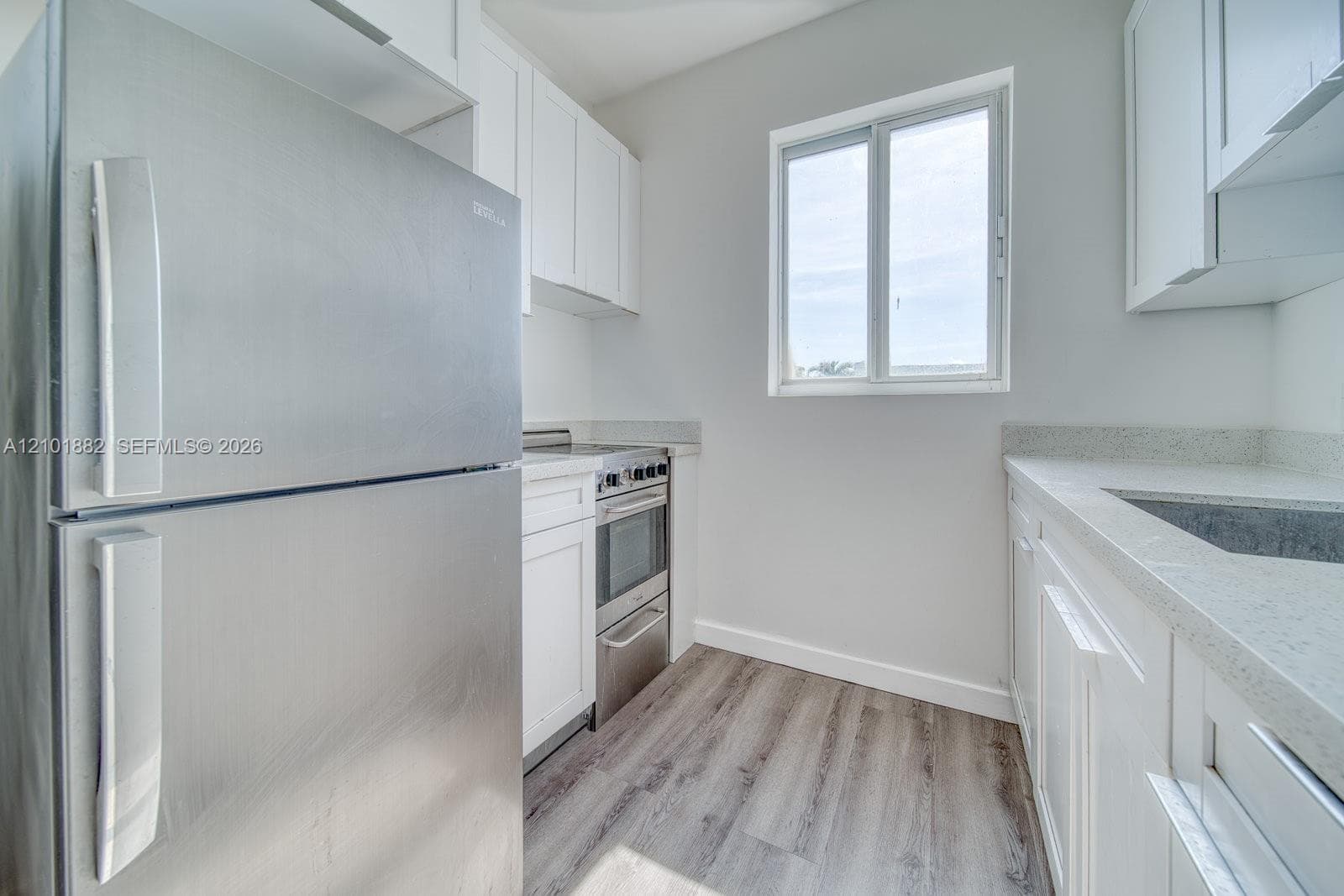 Kitchen featuring white shaker-style cabinetry, stainless steel appliances, speckled stone-finish countertops, and wood-finish flooring