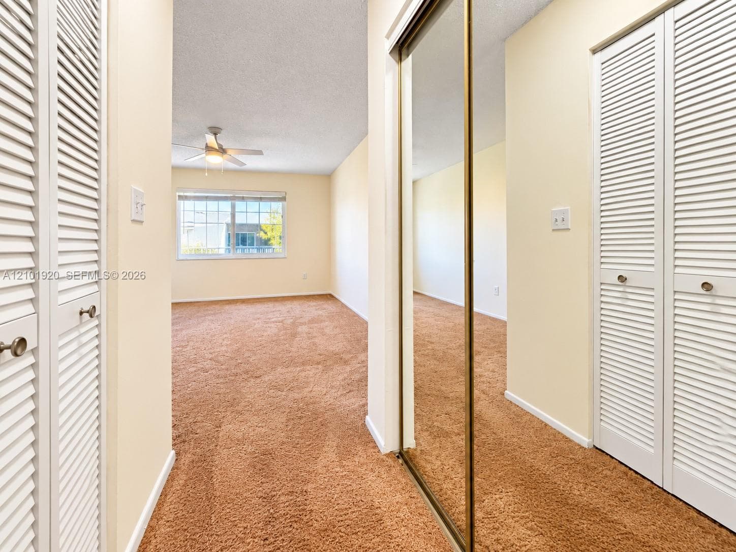 Room featuring dual white louvered-door closets, a mirrored sliding-door closet, wall-to-wall carpeting, and a ceiling fan