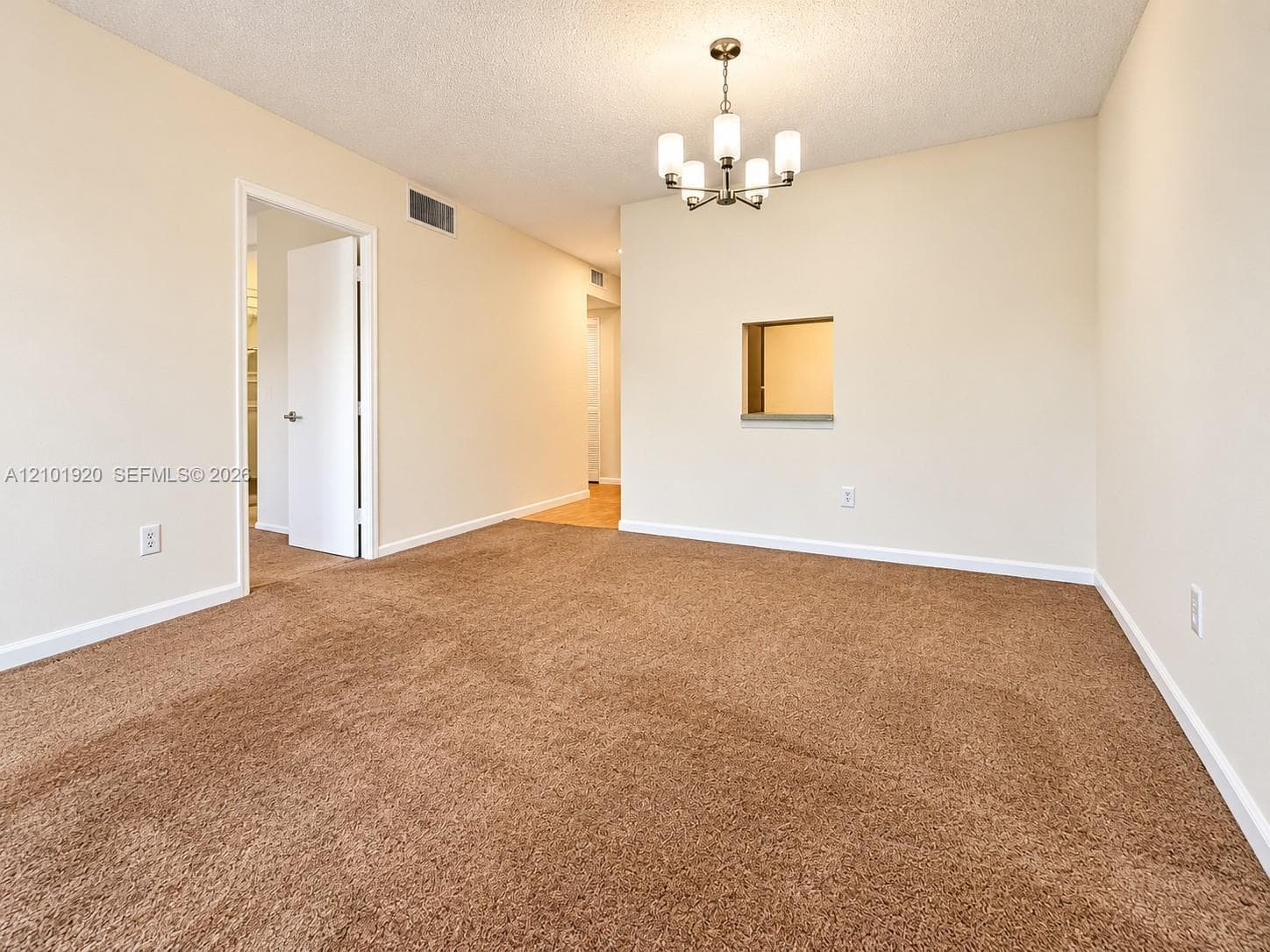 Interior space featuring neutral wall tones, wall-to-wall carpeting, a five-light chandelier, and a decorative interior pass-through window