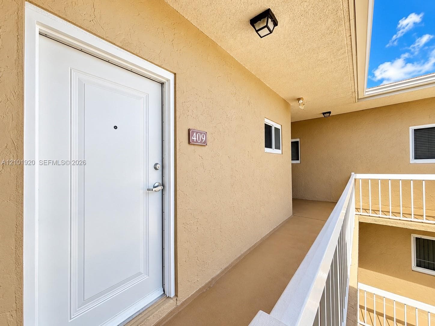 Entryway featuring a white paneled door with a metallic deadbolt, exterior wall-mounted lighting, and a white metal safety railing