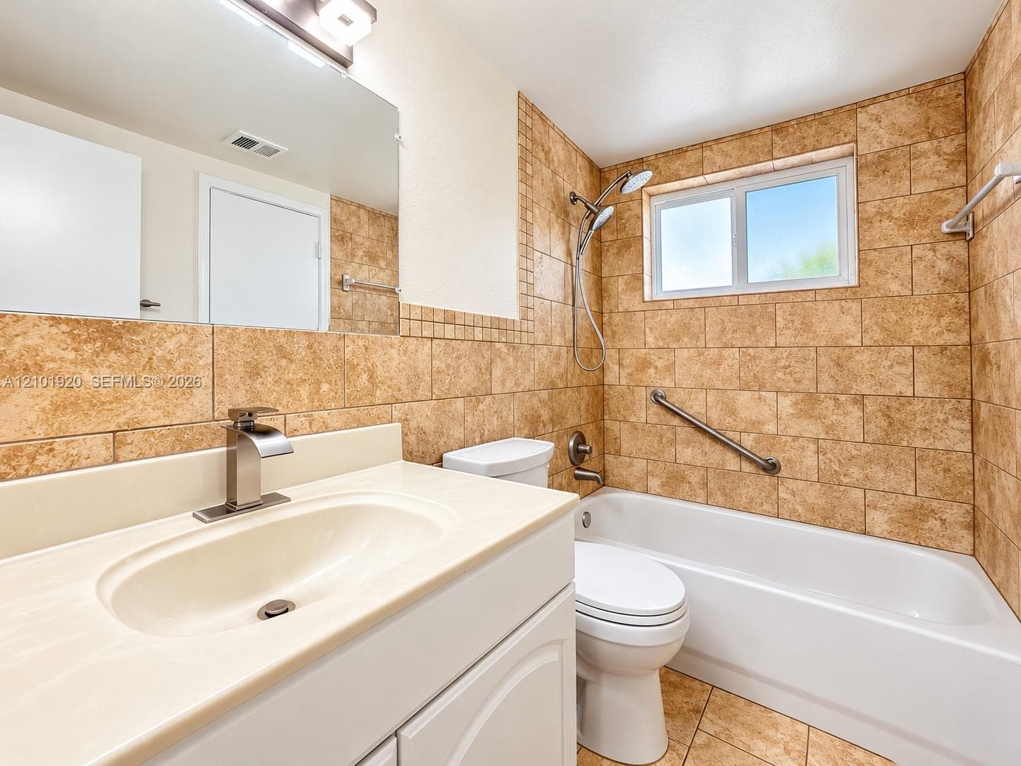 Bathroom featuring a white vanity with a solid surface countertop, an undermount sink, a tub-shower combination with floor-to-ceiling tile surround, and a wall-mounted grab bar