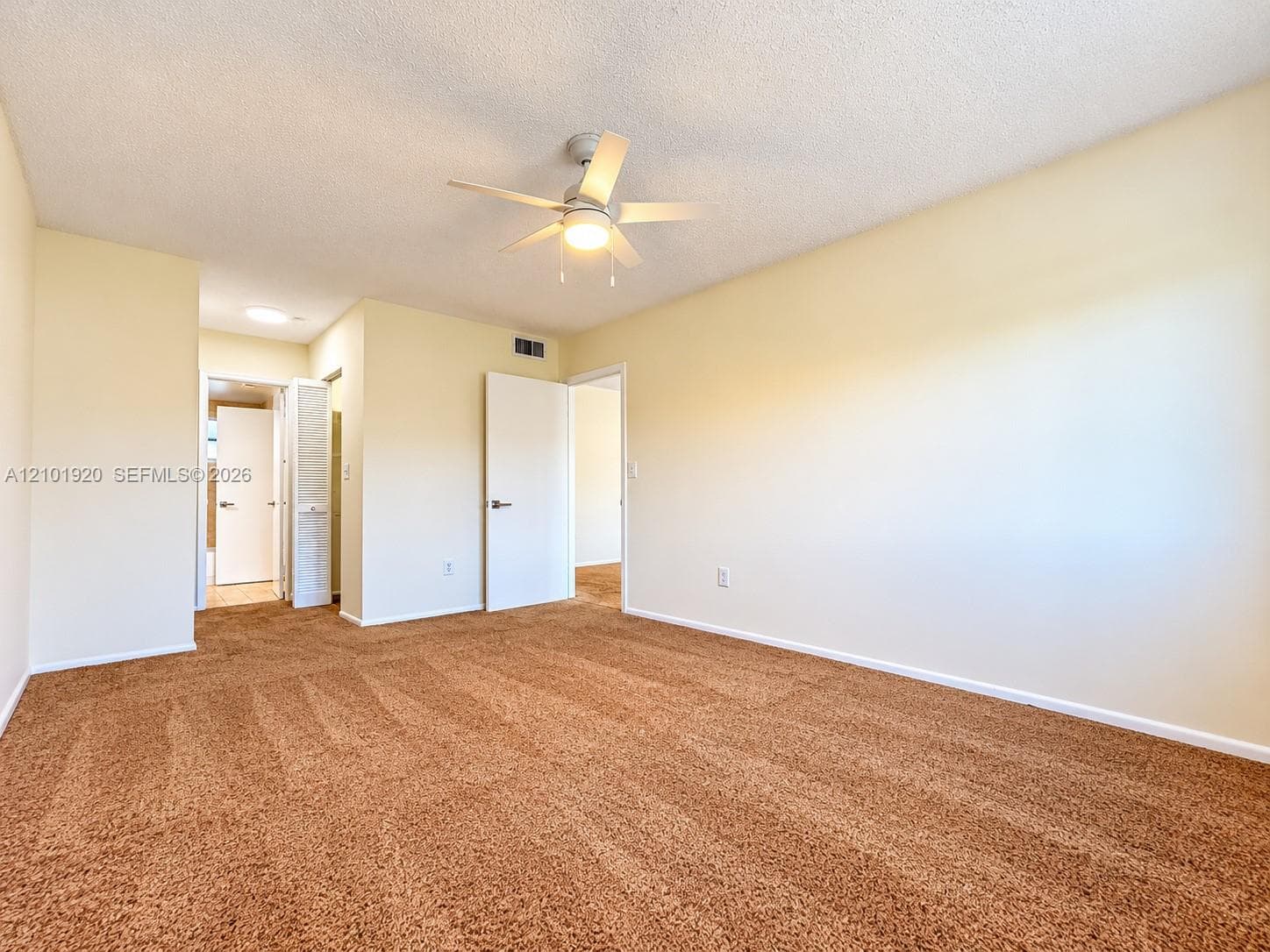 Neutral wall paint, plush carpeting, ceiling fan with integrated lighting, and interior swing doors