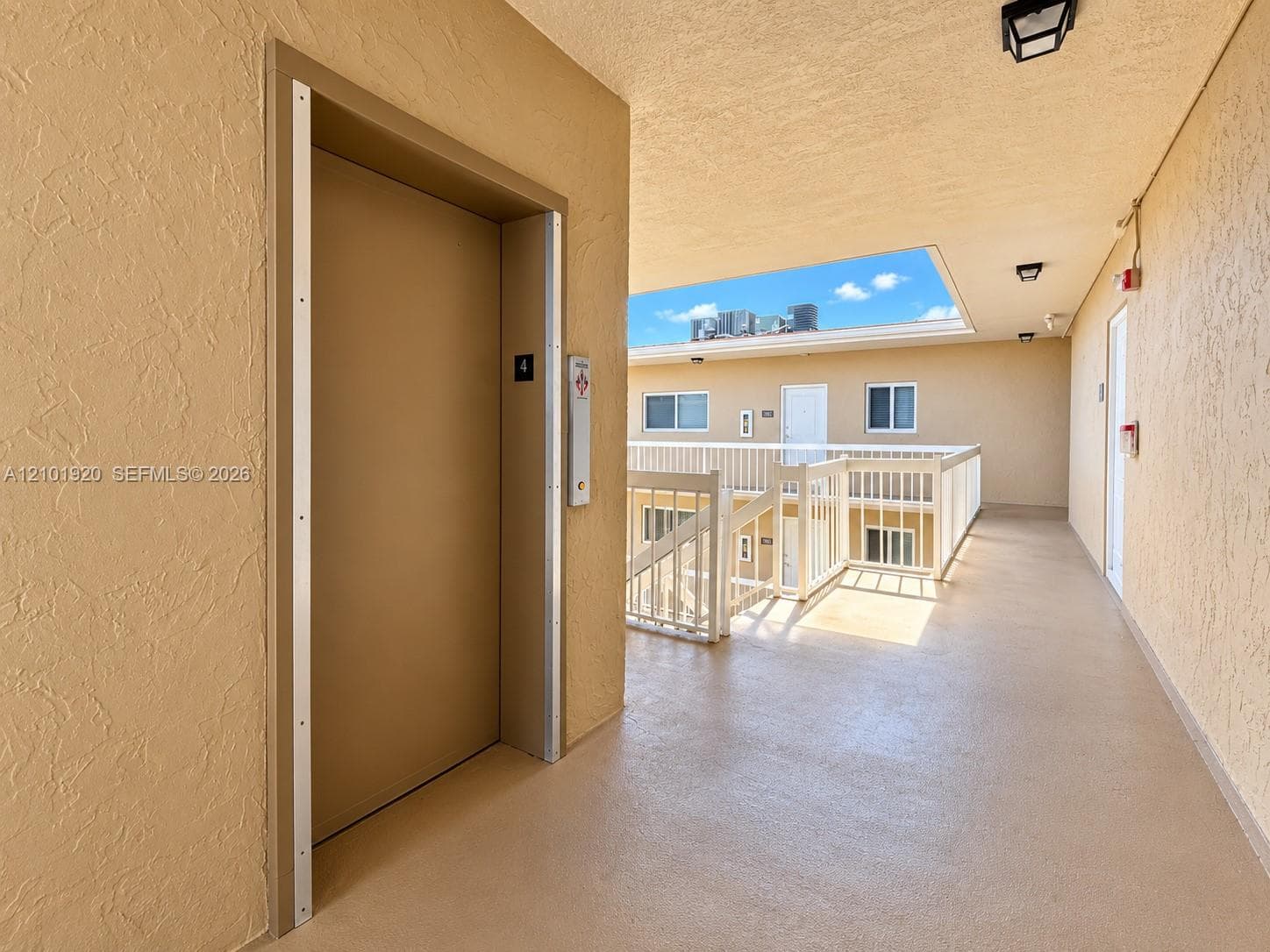 Elevator access with metal door frame, textured exterior walls, and white railing balcony system