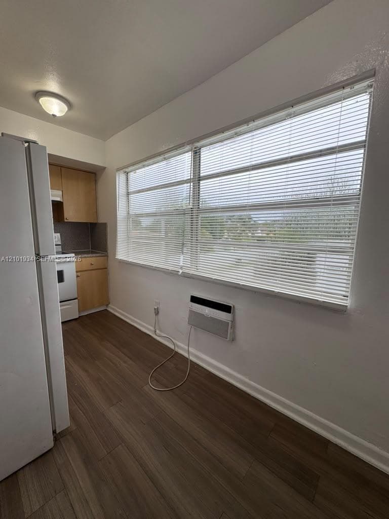 Kitchen featuring wood-finish flooring, light wood cabinetry, white appliances, and a wall-mounted air conditioning unit