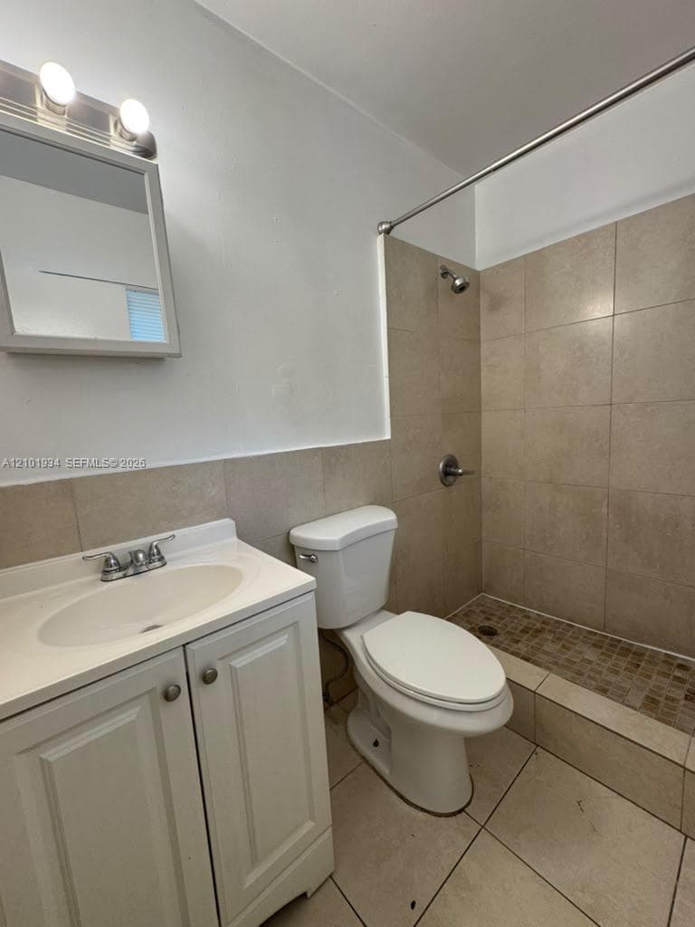Bathroom featuring a white vanity cabinet, a recessed sink, tiled walk-in shower with stone-style mosaic flooring, and a mirrored medicine cabinet with integrated lighting
