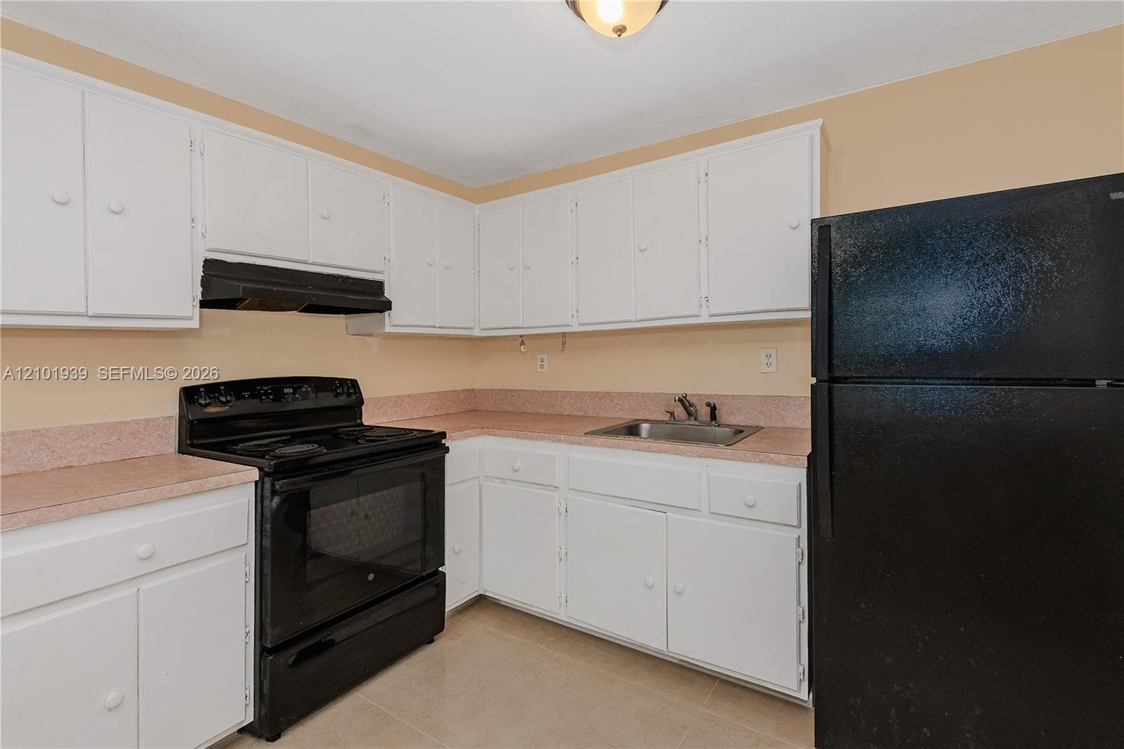 Kitchen featuring white shaker-style cabinetry, solid-surface countertops with integrated backsplash, a black range with hood, and a drop-in stainless steel sink