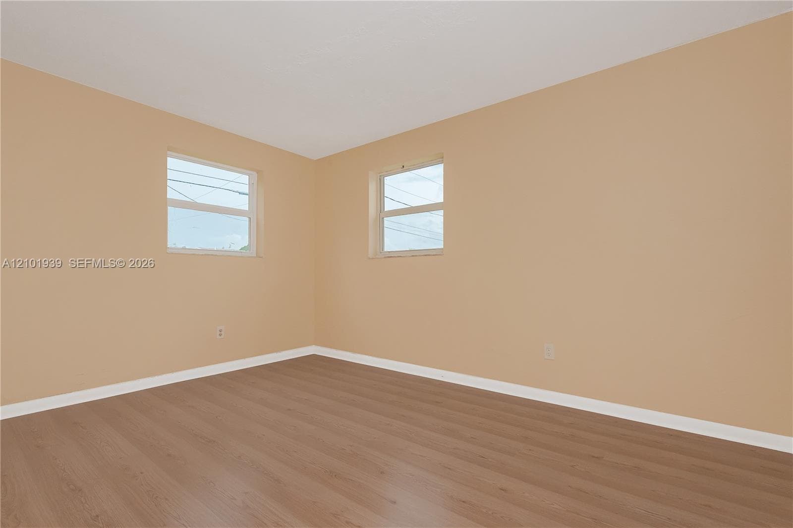 Interior room featuring light-toned neutral wall paint, wood-finish flooring, and dual single-hung windows