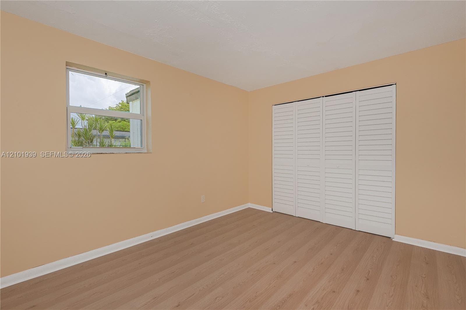 Room interior featuring wood-finish flooring, a single-hung window, and white louvered bifold closet doors