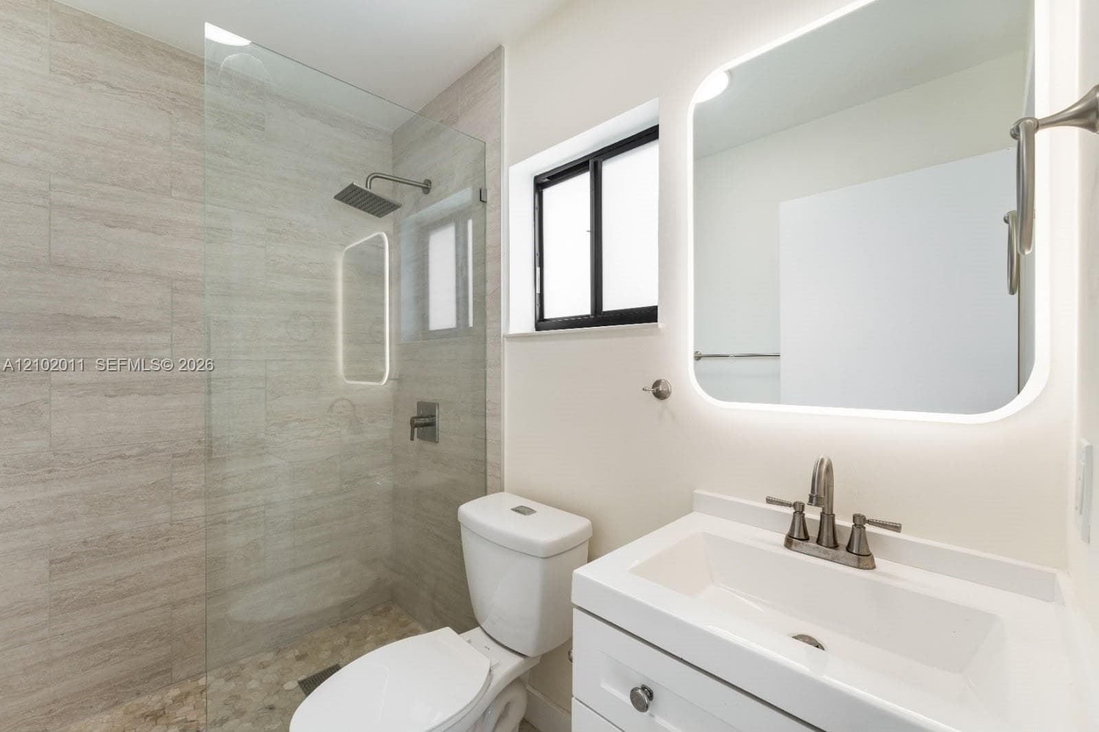 Glass-enclosed shower with rain showerhead, pebble-tiled shower floor, and tiled walls