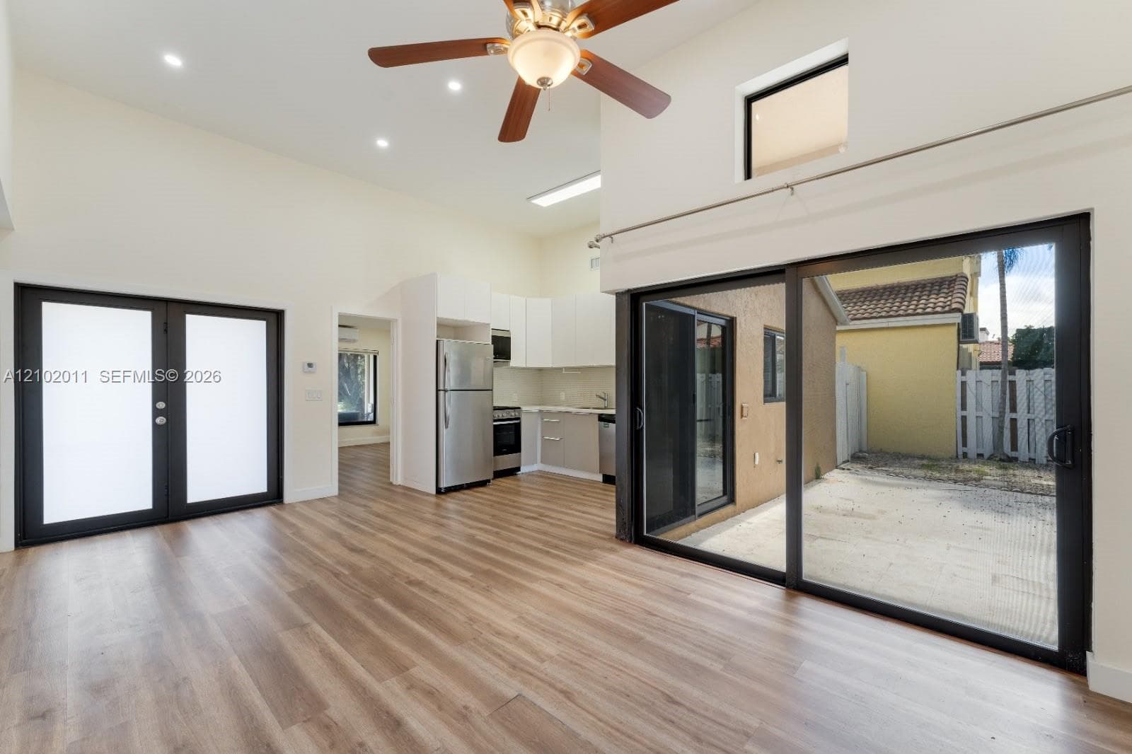 Vaulted ceilings with recessed lighting, wood-finish flooring, sliding glass doors to outdoor space, stainless steel appliances, and white cabinetry with a light-colored countertop