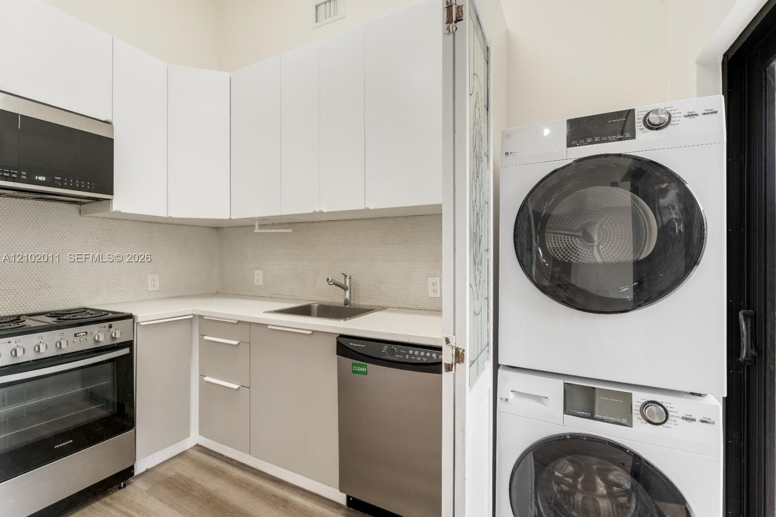 Kitchen featuring stainless steel appliances, a built-in microwave, a stainless steel sink, and white flat-panel cabinetry